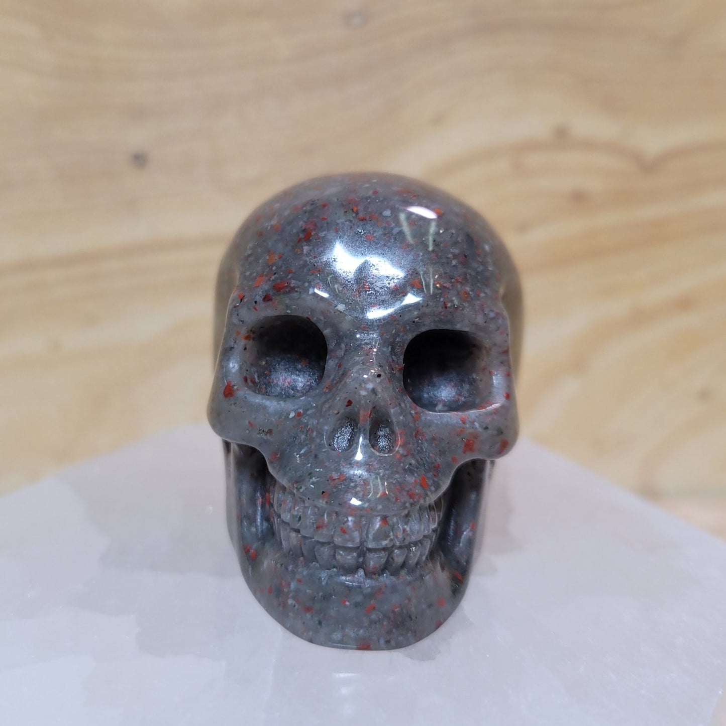 An intricately carved African bloodstone skull, showcasing rich green colors with vibrant red flecks, displayed against a soft, neutral background. This unique piece symbolizes courage, strength, and wisdom, making it an eye-catching decorative item.