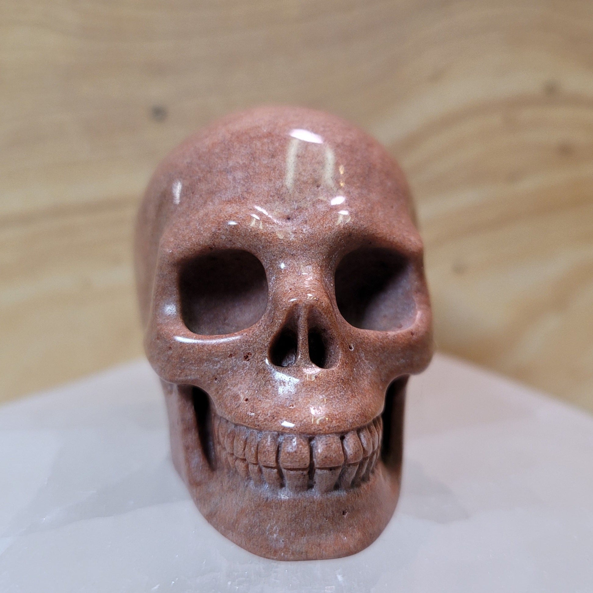  An intricately carved Agate Skull, featuring natural banding and vibrant colors of brown, cream, and gray, displayed against a soft, neutral background. This unique piece symbolizes emotional balance, wisdom, and introspection, making it an eye-catching decorative item.