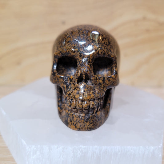 Brown snowflake obsidian skull featuring intricate patterns resembling snowflakes against a light background, known for its grounding and protective metaphysical properties.