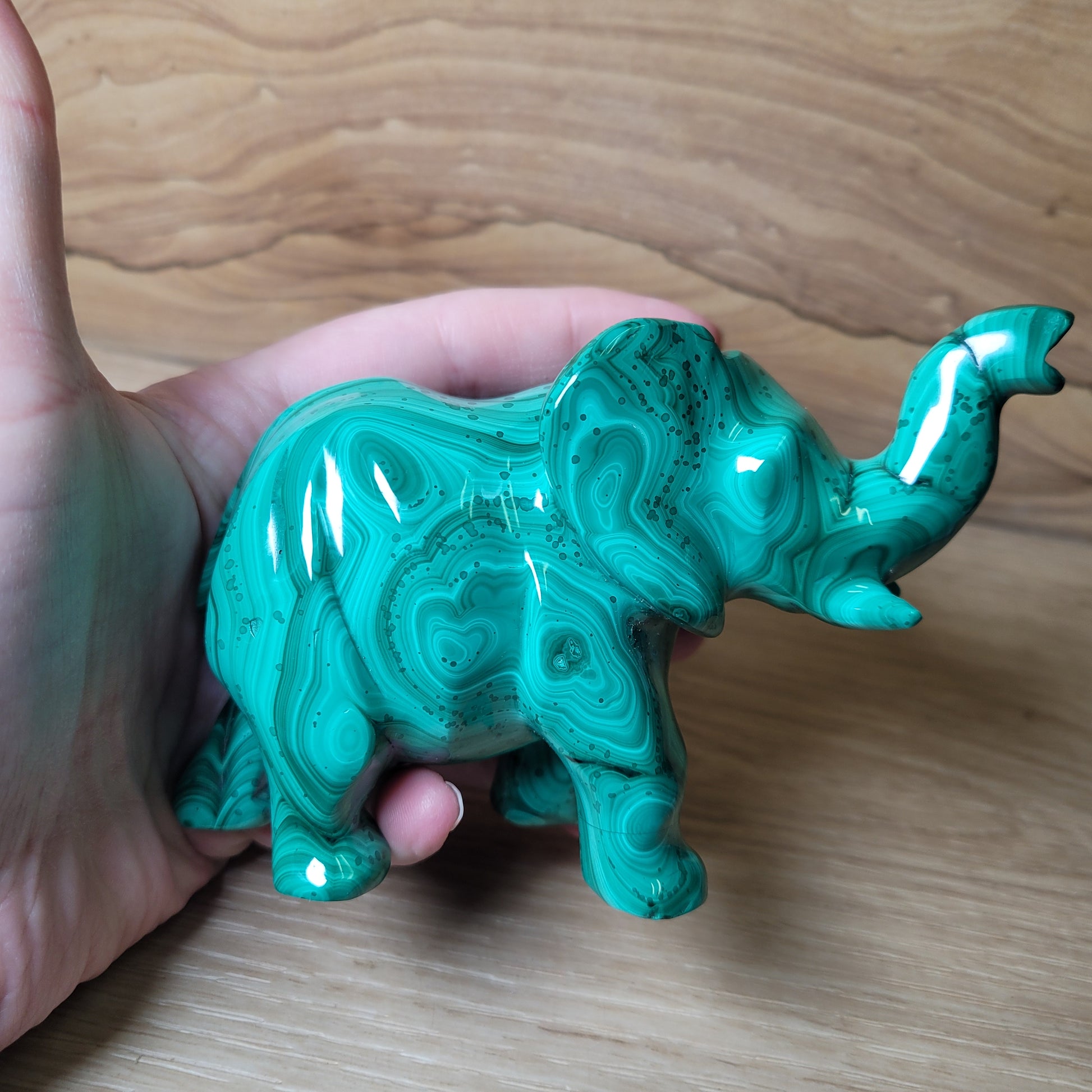 Green Malachite elephant carving held in a hand on a wooden surface