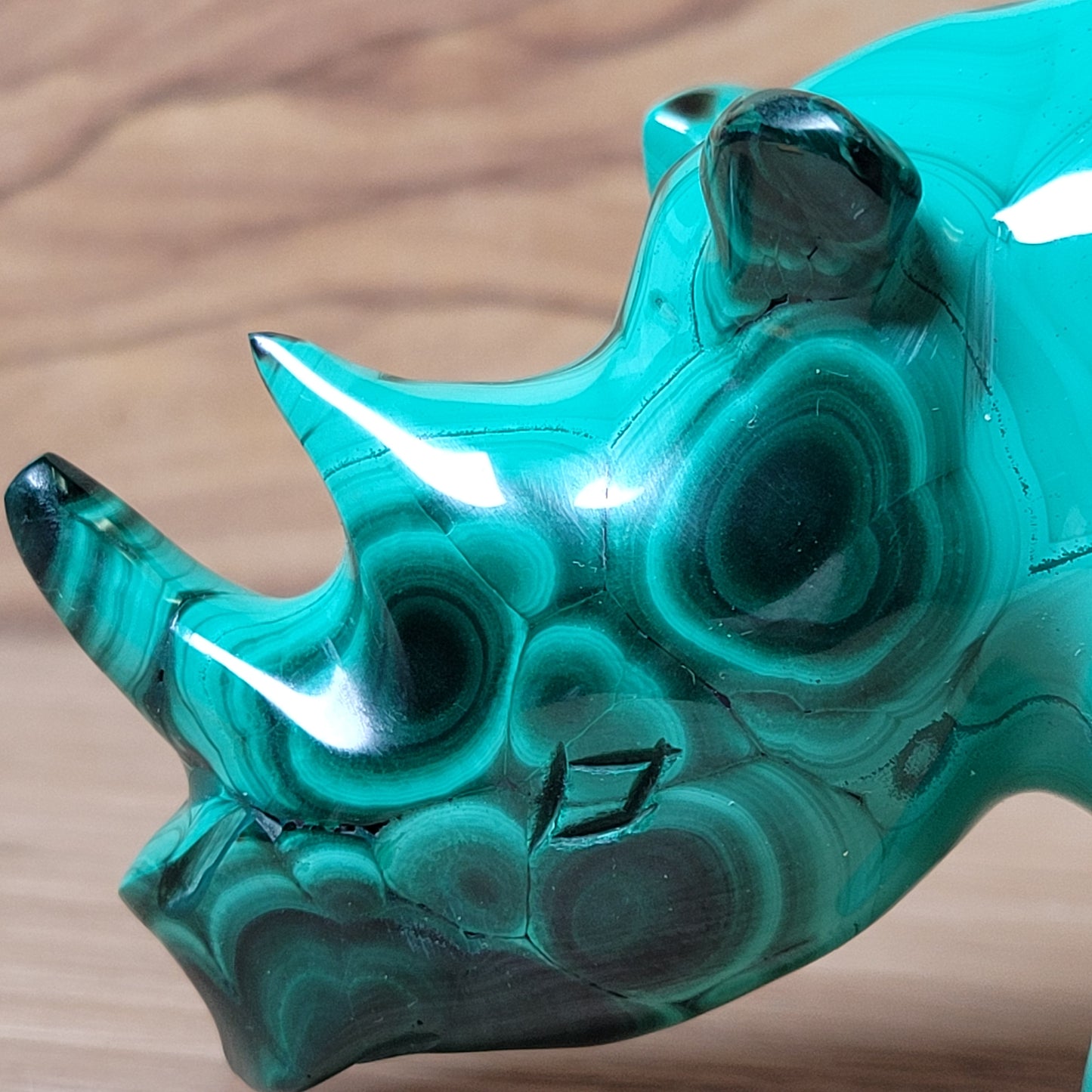 Green Malachite rhinoceros carving on a wooden surface