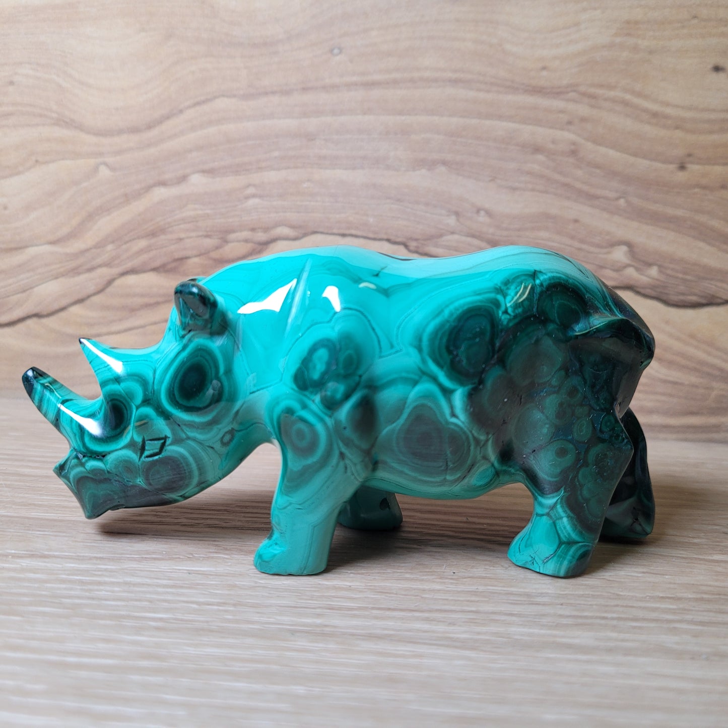 Green Malachite rhinoceros carving on a wooden surface