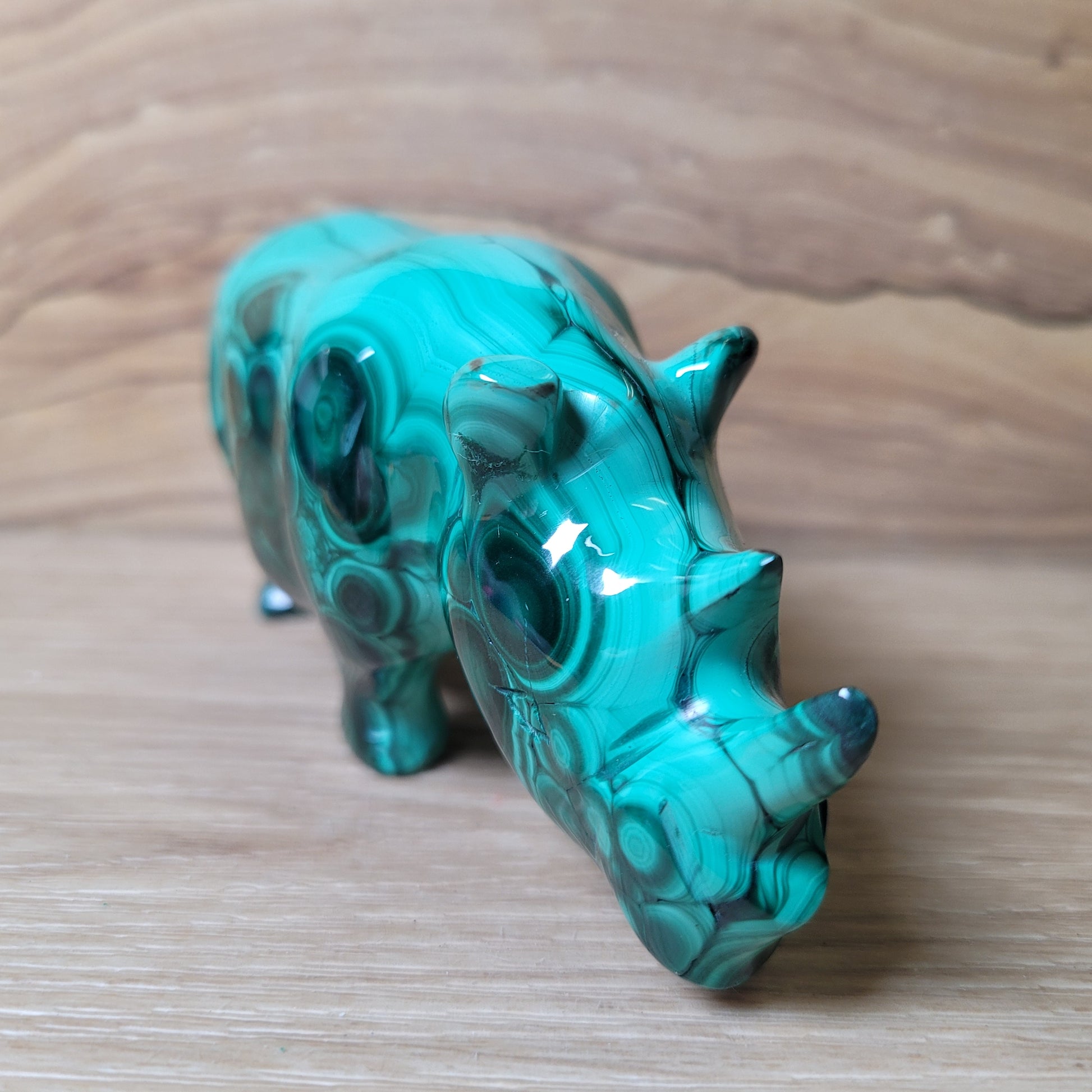 Green Malachite rhinoceros carving on a wooden surface
