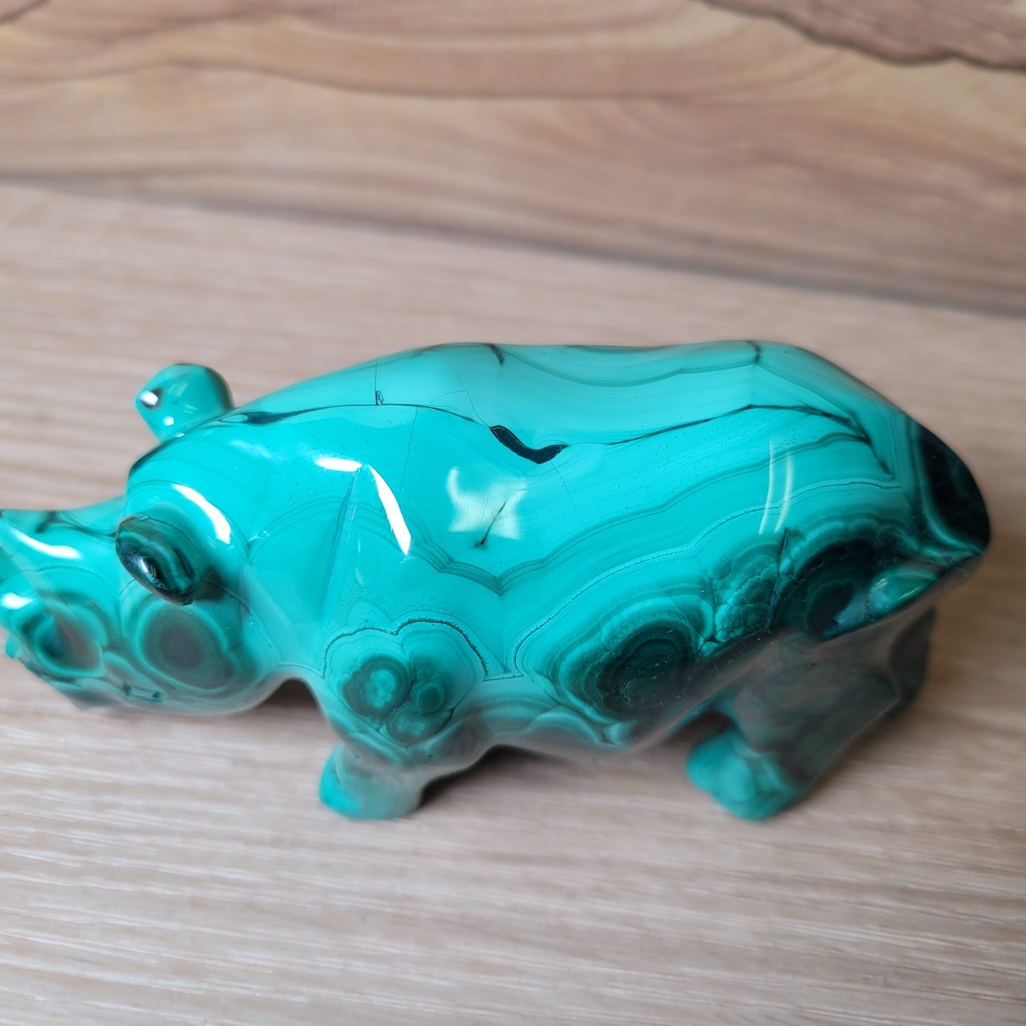 Green Malachite rhinoceros carving on a wooden surface