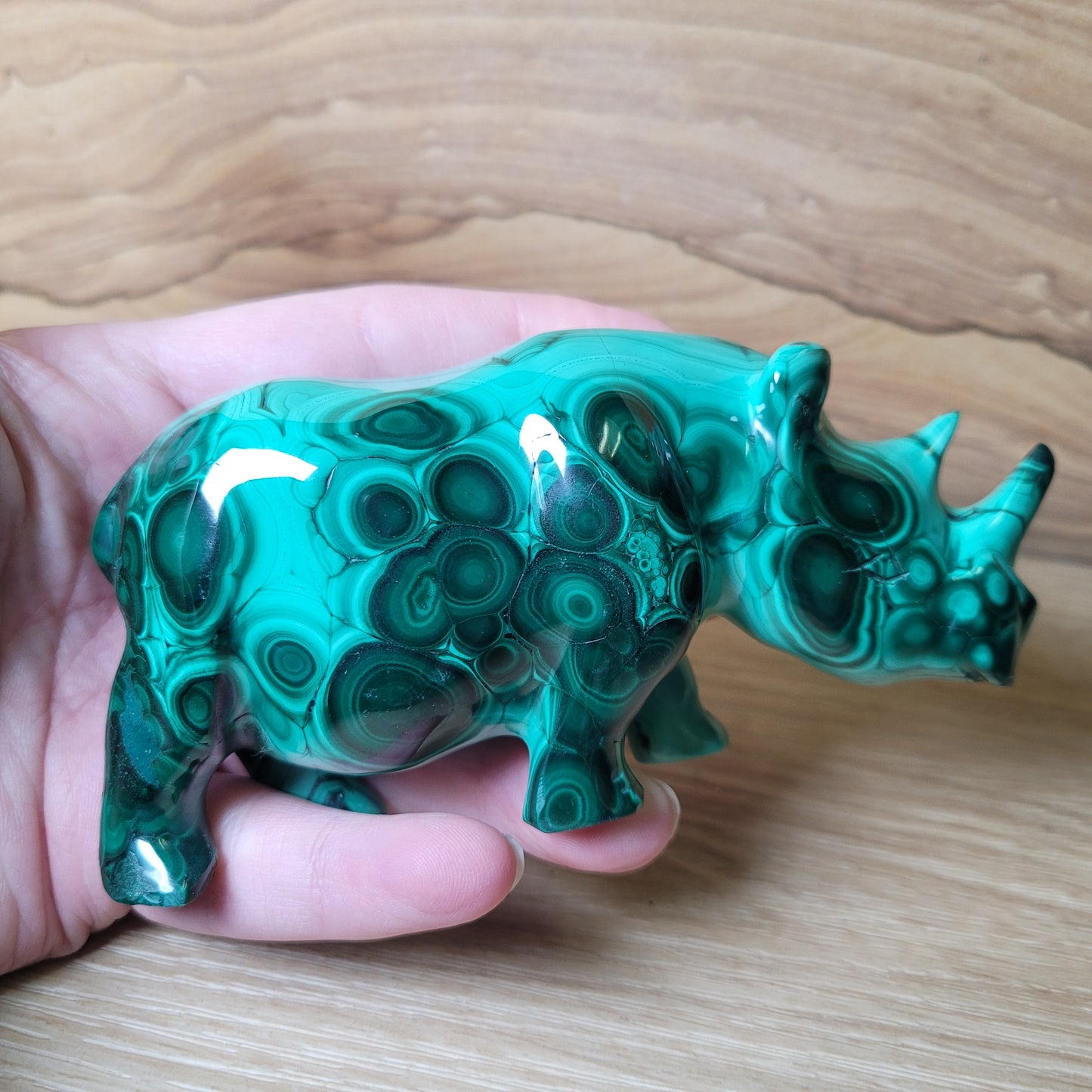 Green rhinoceros figurine held in a hand on a wooden surface