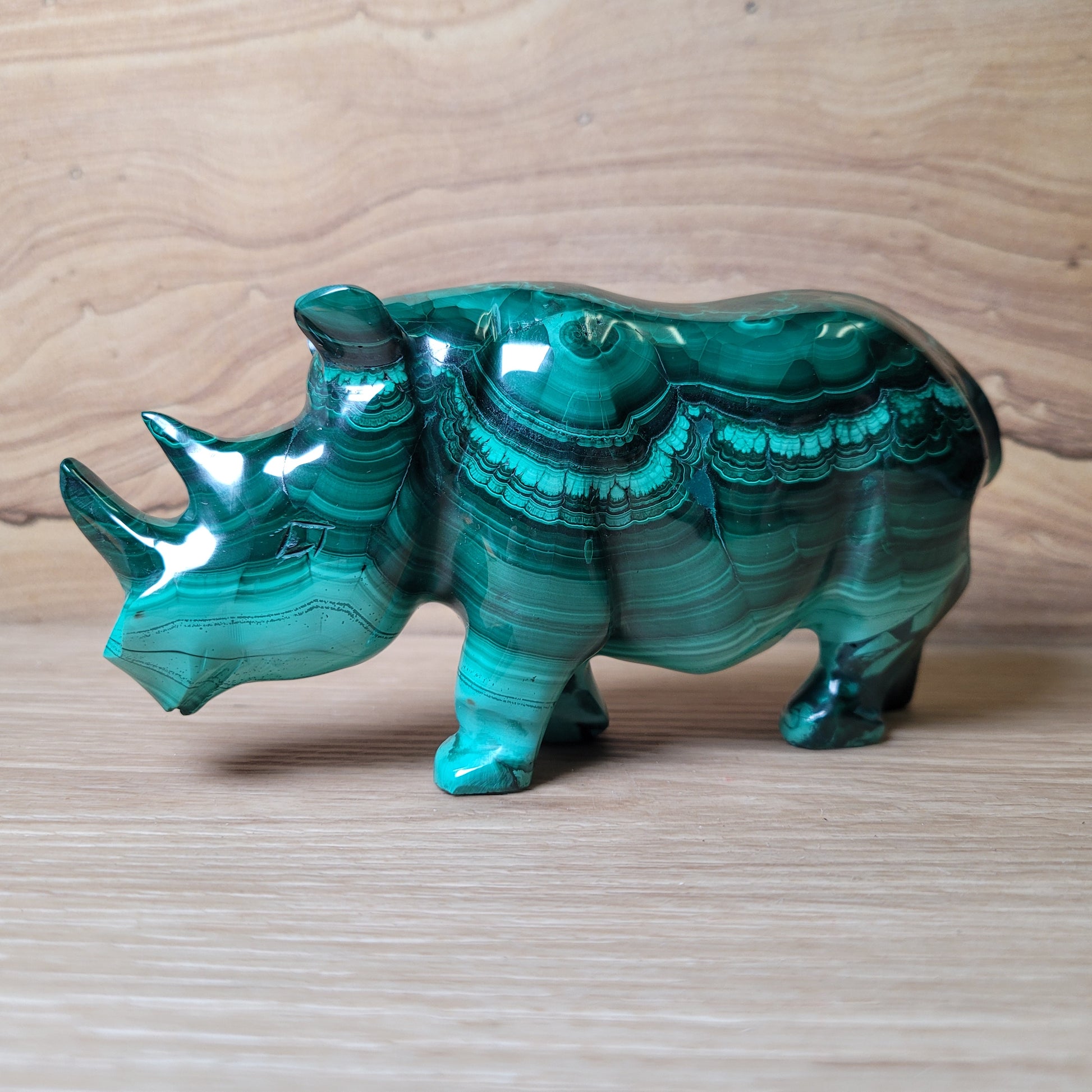Green malachite rhinoceros carving on a wooden surface