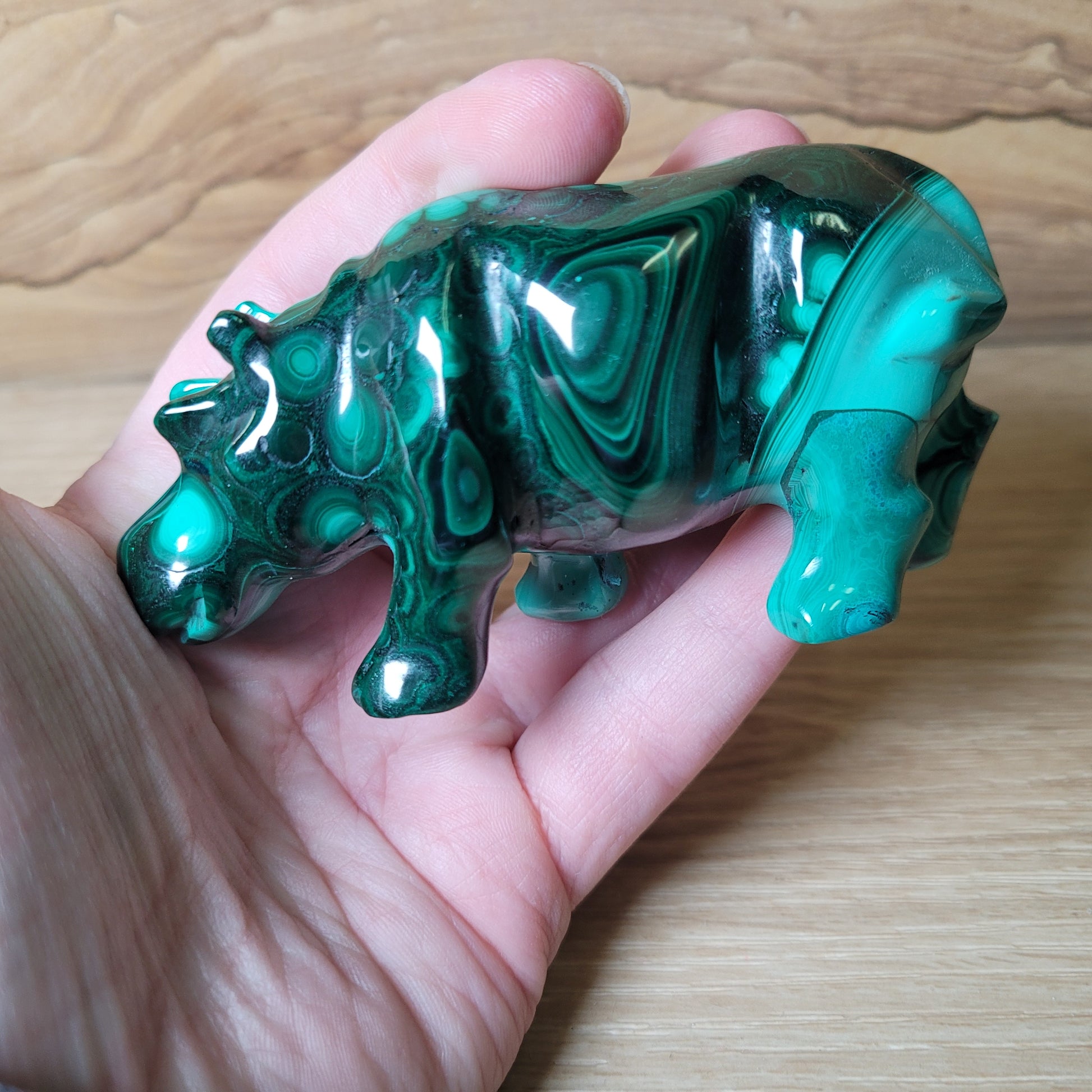 Green Malachite stone hippopotamus held in a hand on a wooden surface