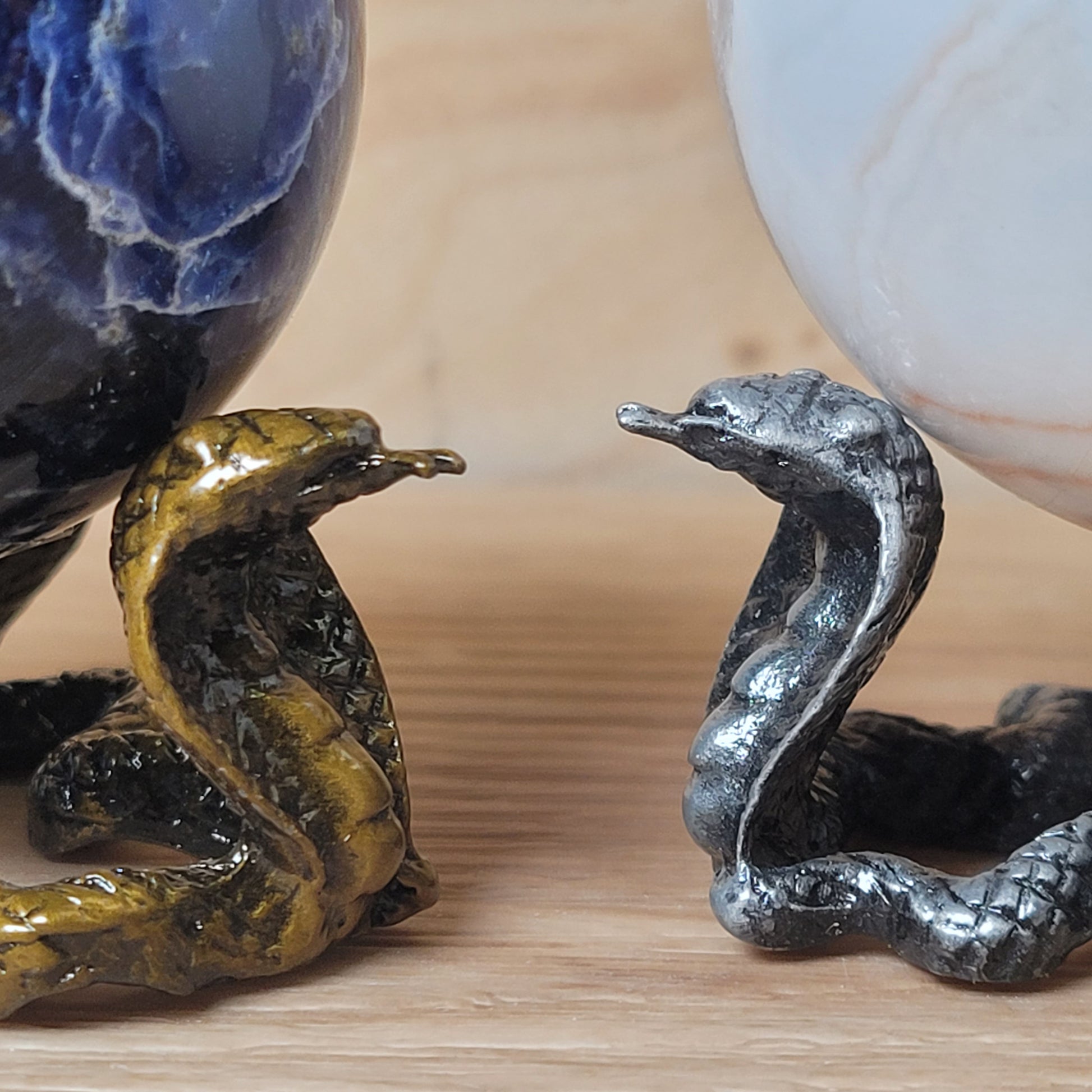 Two snake-shaped objects, one gold and one silver, on a wooden surface.