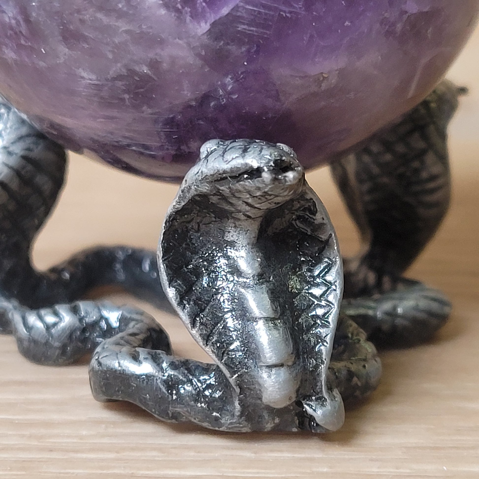 Metallic snake figurine on a wooden surface with a large purple crystal in the background