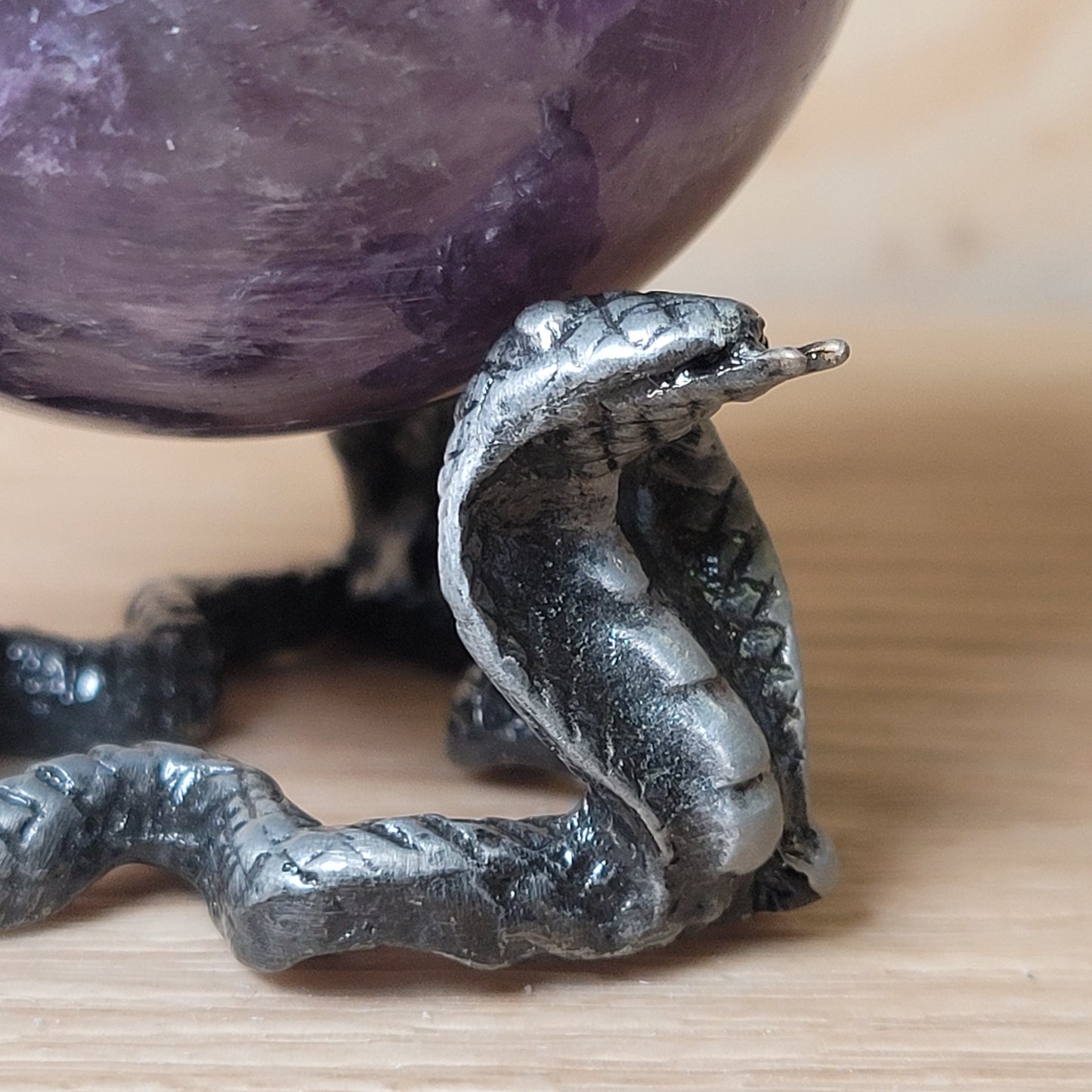 Metallic snake figurine on a wooden surface with a purple crystal in the background