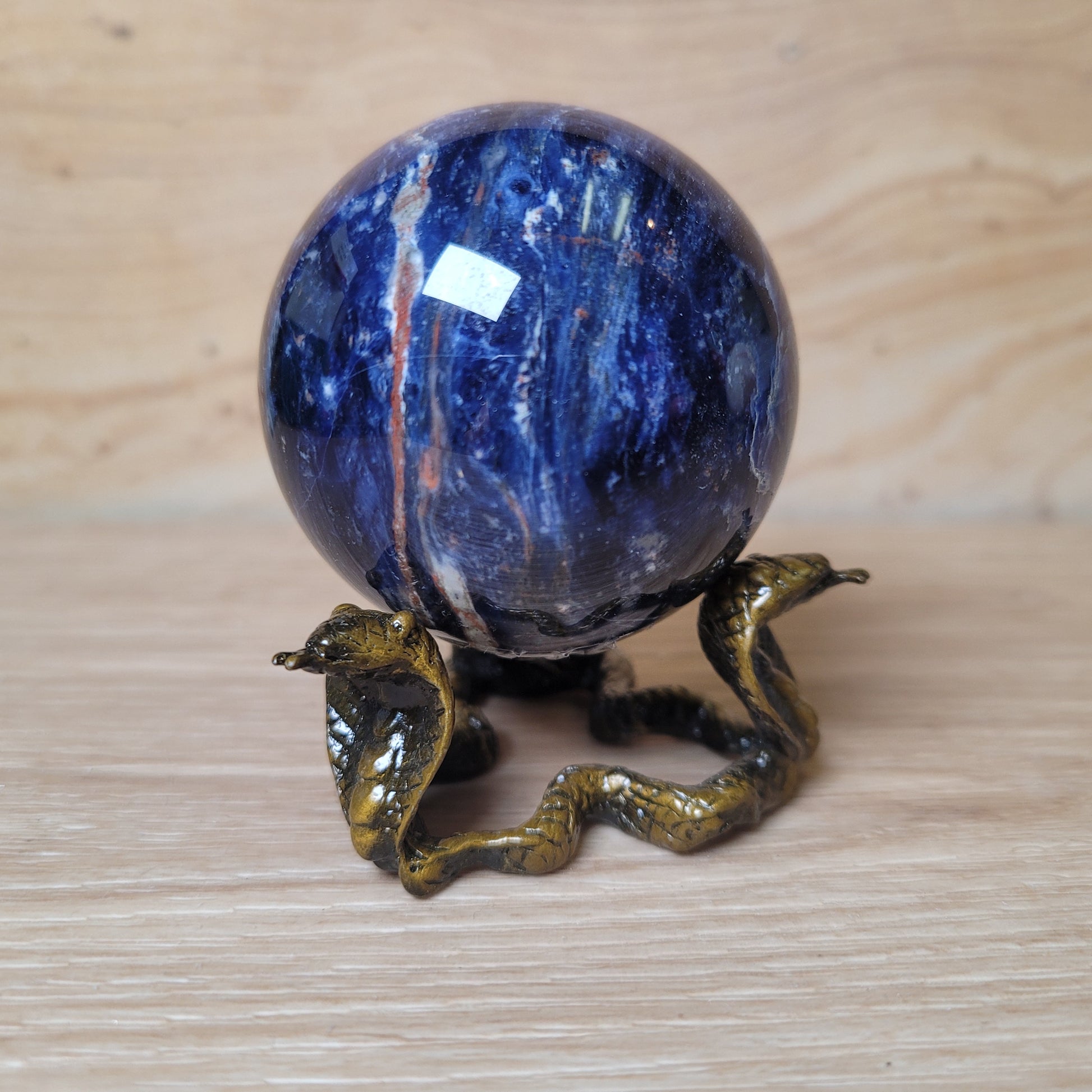 Blue marbled sphere with a bronze snake on a wooden surface